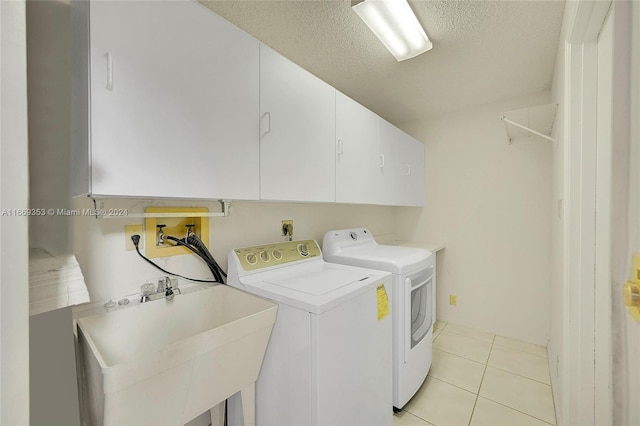 clothes washing area featuring light tile patterned flooring, a textured ceiling, cabinets, washer and clothes dryer, and sink