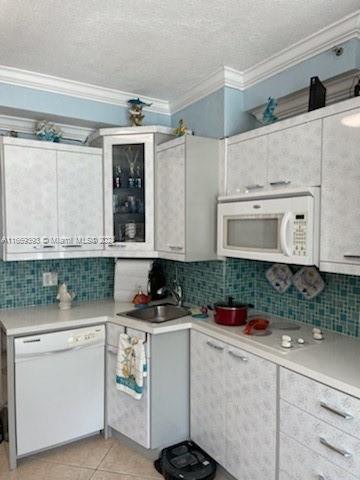 kitchen with a textured ceiling, light tile patterned flooring, white cabinetry, white appliances, and ornamental molding