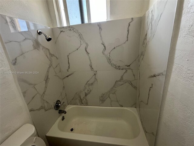 bathroom featuring tiled shower / bath combo and toilet