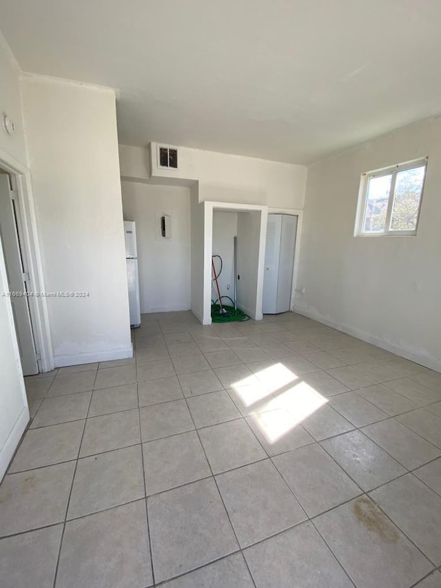 unfurnished bedroom featuring light tile patterned flooring and white fridge