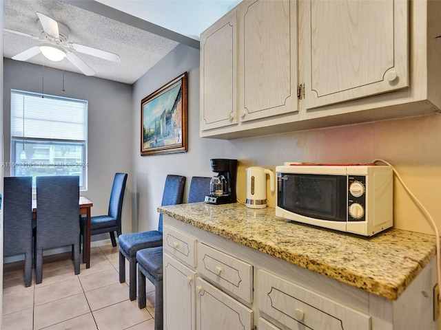 kitchen featuring ceiling fan, light tile patterned flooring, a textured ceiling, light brown cabinetry, and light stone countertops