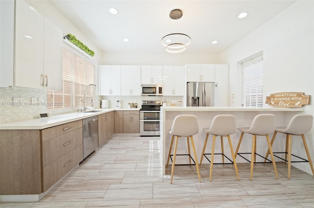 kitchen featuring appliances with stainless steel finishes, a kitchen breakfast bar, sink, decorative light fixtures, and white cabinetry