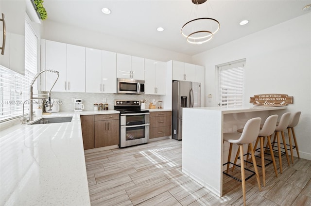 kitchen featuring white cabinetry, plenty of natural light, stainless steel appliances, and decorative light fixtures