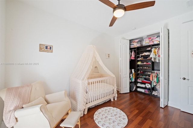 bedroom featuring ceiling fan, a crib, dark wood-type flooring, and a closet