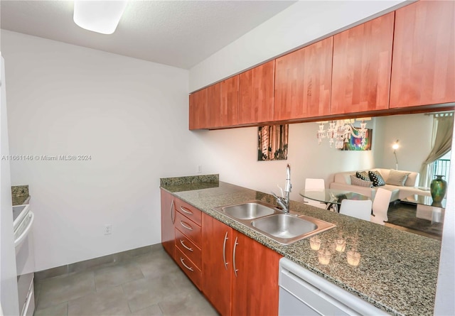 kitchen with an inviting chandelier, dishwasher, dark stone counters, and sink