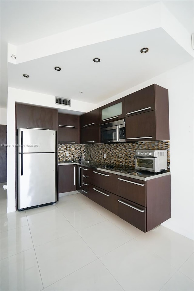 kitchen featuring backsplash, dark brown cabinets, light tile patterned floors, and stainless steel appliances