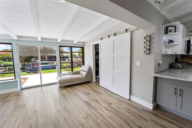 interior space featuring light hardwood / wood-style flooring, lofted ceiling with beams, and a barn door