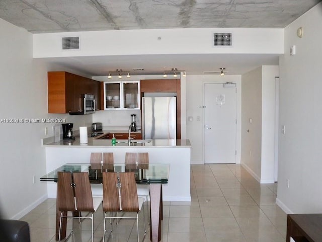 kitchen featuring sink, kitchen peninsula, a kitchen bar, stainless steel appliances, and light tile patterned floors