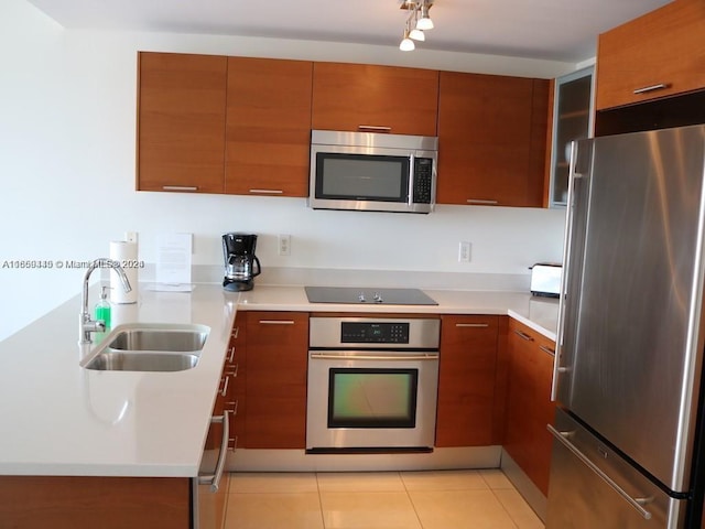 kitchen featuring appliances with stainless steel finishes, light tile patterned floors, brown cabinets, and a sink
