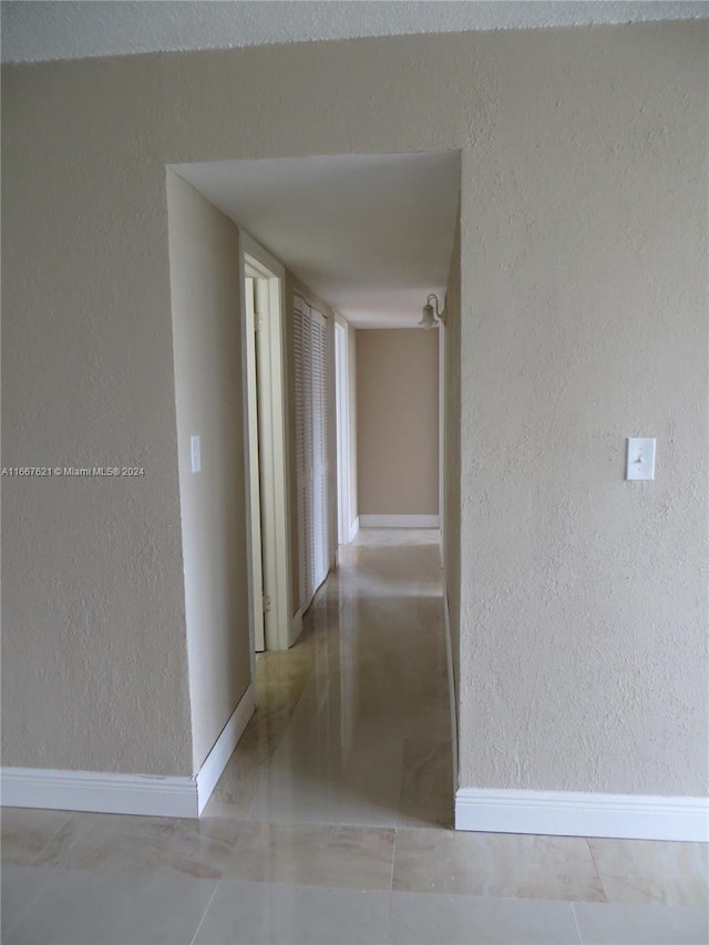 hallway featuring baseboards and a textured wall