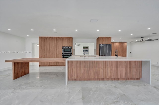 kitchen featuring fridge, double oven, a large island with sink, and sink