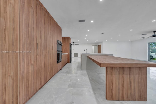 kitchen with ceiling fan, stainless steel fridge, sink, a large island, and black double oven