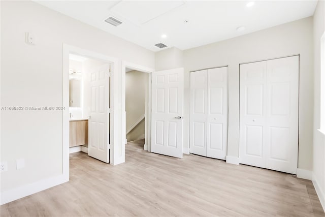 unfurnished bedroom with ensuite bath, multiple closets, and light wood-type flooring