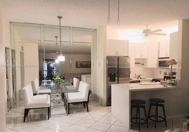 kitchen featuring ceiling fan, stainless steel appliances, hanging light fixtures, white cabinetry, and a textured ceiling