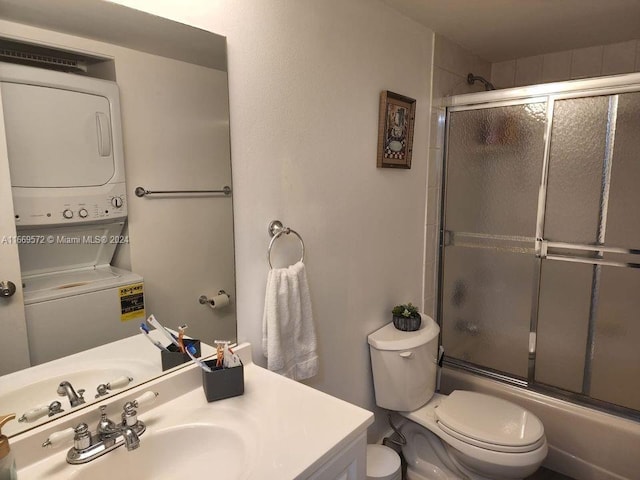 full bathroom featuring stacked washer and dryer, bath / shower combo with glass door, vanity, and toilet