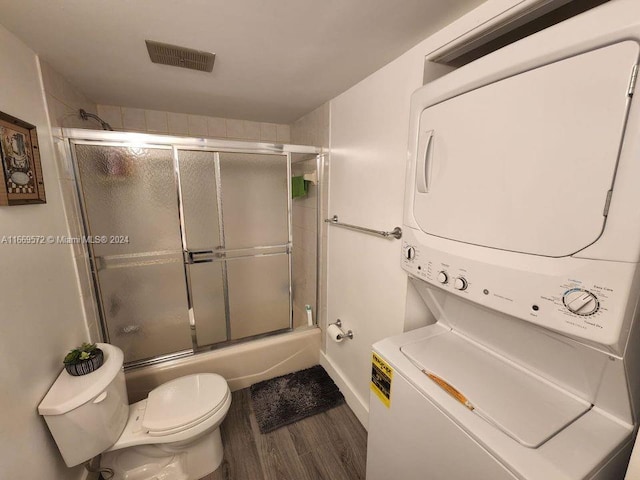 bathroom with wood-type flooring, combined bath / shower with glass door, stacked washer / dryer, and toilet