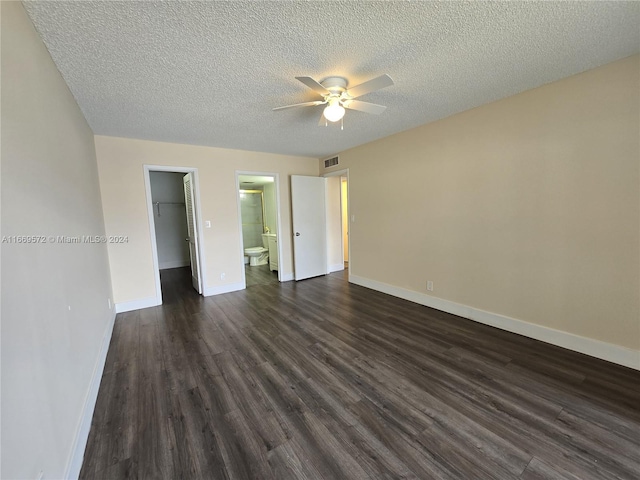 unfurnished bedroom with a spacious closet, connected bathroom, ceiling fan, and dark hardwood / wood-style flooring