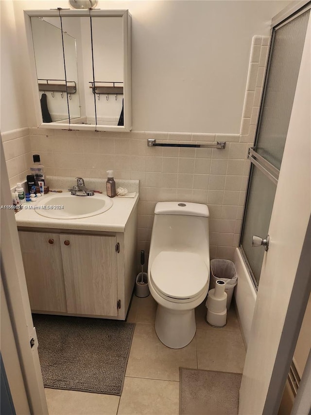 full bathroom with vanity, combined bath / shower with glass door, tile patterned floors, tile walls, and toilet