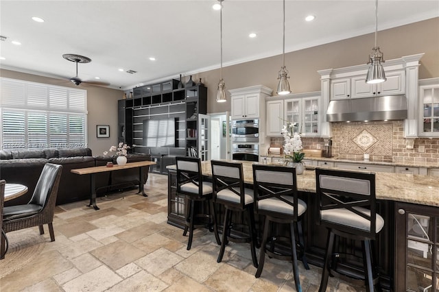 kitchen with a kitchen breakfast bar, hanging light fixtures, white cabinetry, and light stone counters