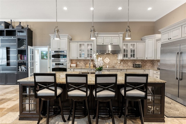 kitchen with appliances with stainless steel finishes, a large island with sink, light stone countertops, and white cabinets