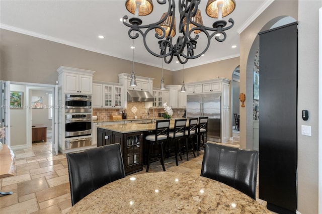 kitchen with appliances with stainless steel finishes, white cabinetry, light stone countertops, crown molding, and a center island