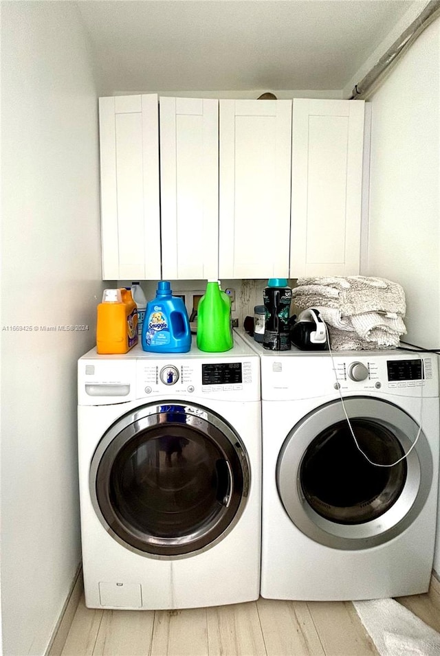 laundry room with light wood-type flooring, separate washer and dryer, and cabinets