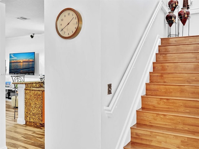 stairway with ornamental molding and hardwood / wood-style floors