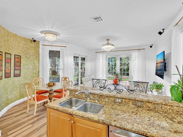 kitchen featuring sink, light wood-type flooring, light stone counters, ornamental molding, and a chandelier