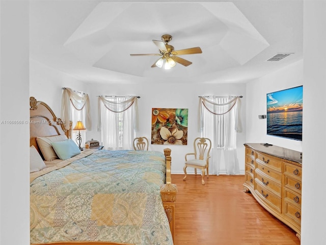 bedroom featuring a raised ceiling, light wood-type flooring, and ceiling fan