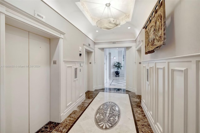 interior space with a raised ceiling, elevator, and a chandelier