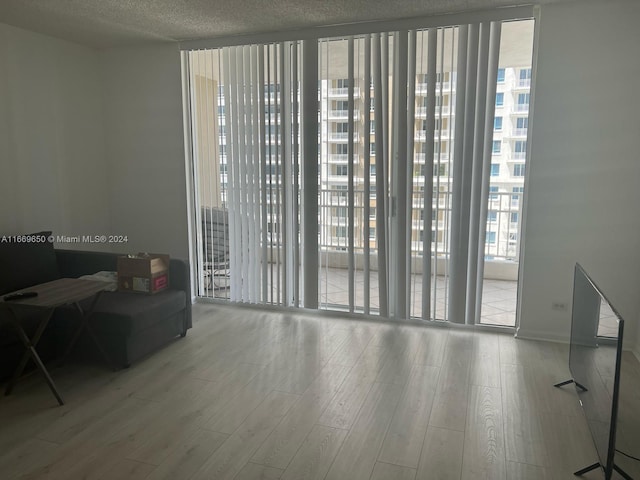 spare room featuring floor to ceiling windows, a wealth of natural light, light hardwood / wood-style floors, and a textured ceiling