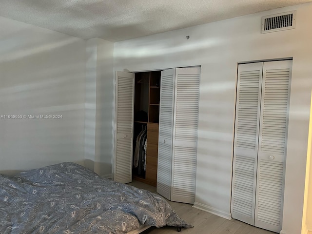 bedroom with multiple closets, a textured ceiling, and light hardwood / wood-style flooring