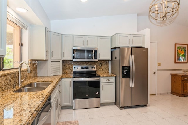 kitchen featuring light stone counters, a sink, vaulted ceiling, appliances with stainless steel finishes, and tasteful backsplash