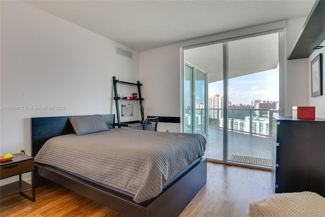 bedroom featuring a wall of windows, a textured ceiling, light hardwood / wood-style flooring, and access to outside