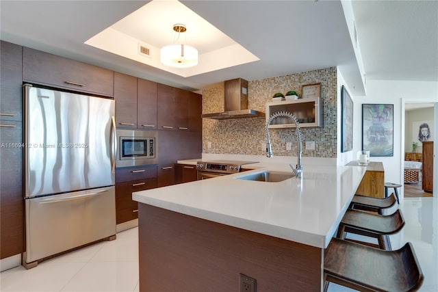 kitchen with decorative light fixtures, sink, a tray ceiling, stainless steel appliances, and wall chimney exhaust hood