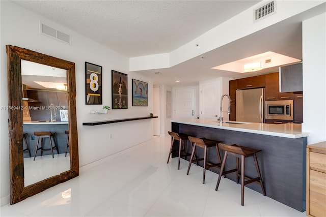 kitchen with a kitchen bar, sink, a textured ceiling, kitchen peninsula, and stainless steel appliances