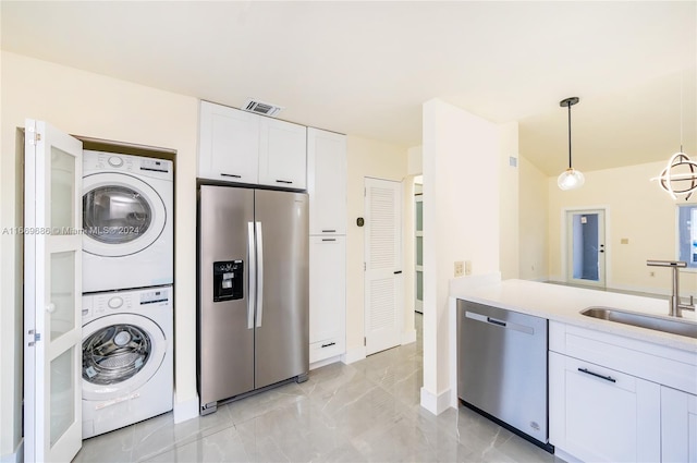 kitchen with pendant lighting, stacked washer and dryer, sink, white cabinets, and appliances with stainless steel finishes