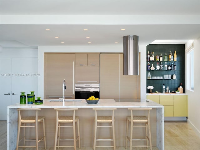 kitchen with oven, a kitchen breakfast bar, sink, and light hardwood / wood-style flooring