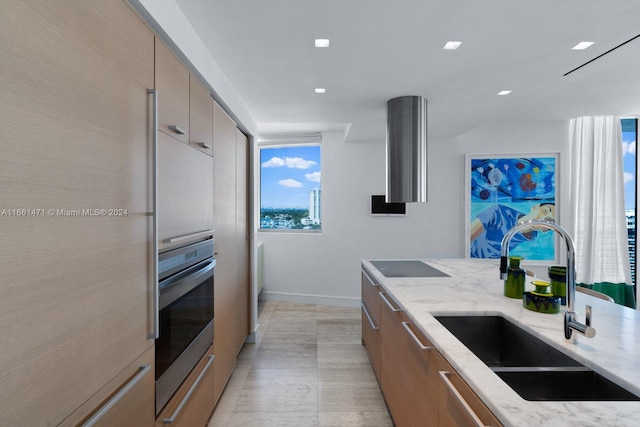 kitchen featuring light stone countertops, light brown cabinetry, sink, and stainless steel oven