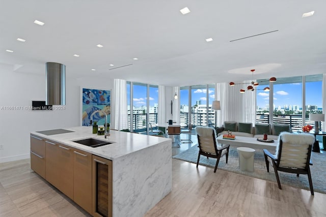 kitchen with floor to ceiling windows, a center island with sink, black electric stovetop, sink, and light stone counters