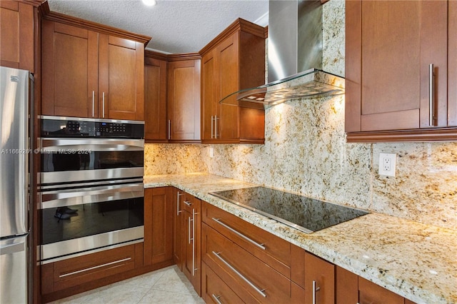 kitchen featuring appliances with stainless steel finishes, a textured ceiling, light stone countertops, and wall chimney range hood