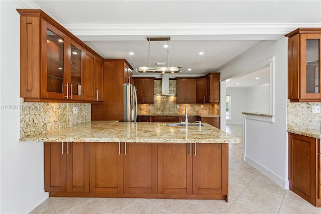 kitchen with ornamental molding, kitchen peninsula, wall chimney range hood, stainless steel refrigerator, and light stone countertops