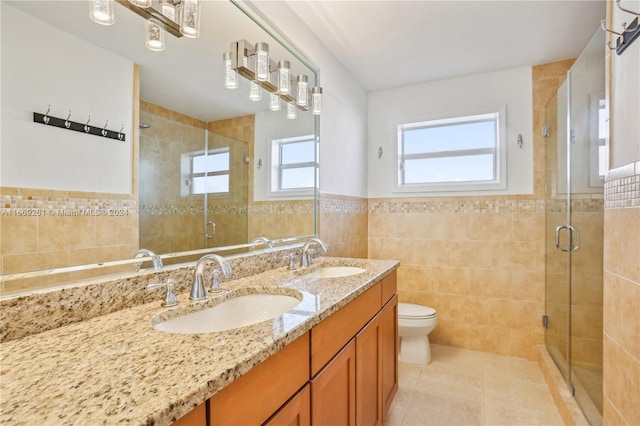 bathroom with tile walls, a shower with door, tile patterned floors, vanity, and toilet