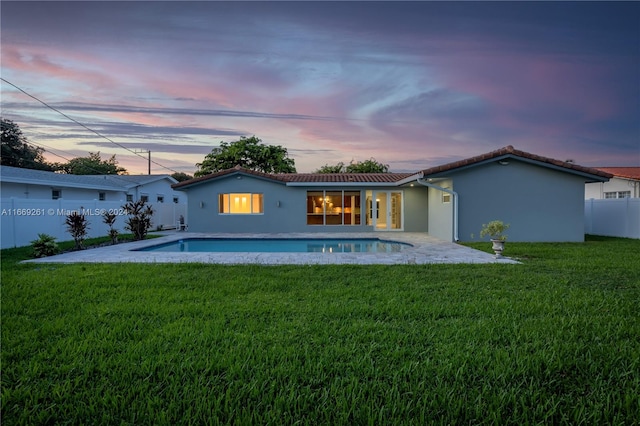 back house at dusk featuring a fenced in pool, a lawn, and a patio