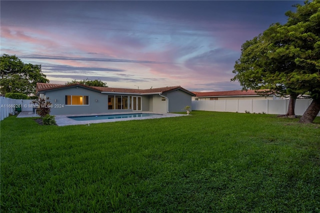 back house at dusk featuring a lawn and a patio area