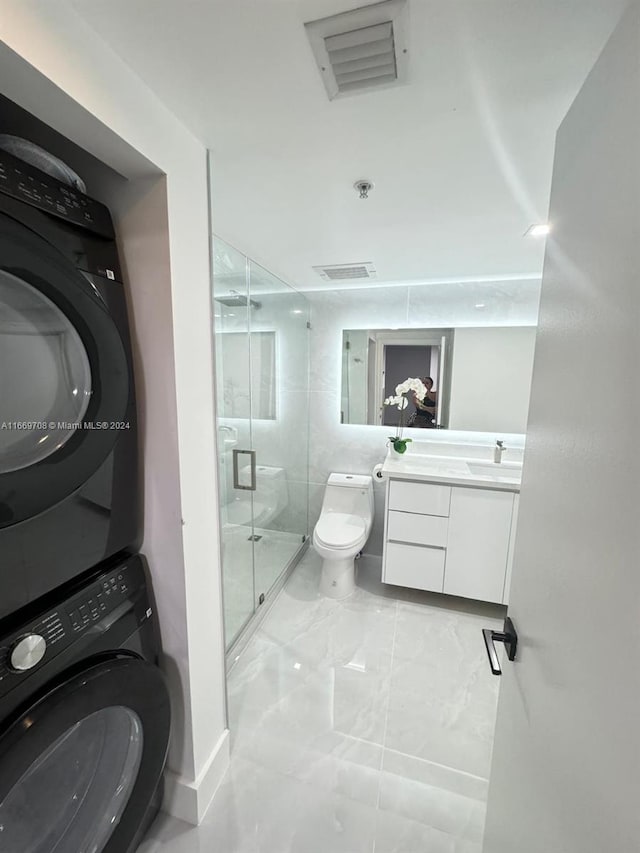 bathroom featuring stacked washer and clothes dryer, vanity, toilet, and a shower with door