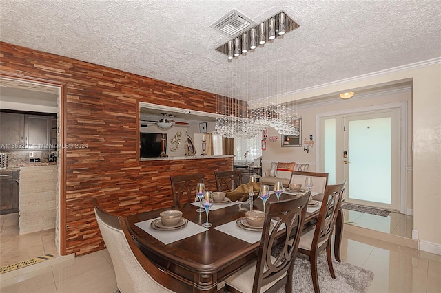 tiled dining space with ceiling fan with notable chandelier, wooden walls, a textured ceiling, and ornamental molding