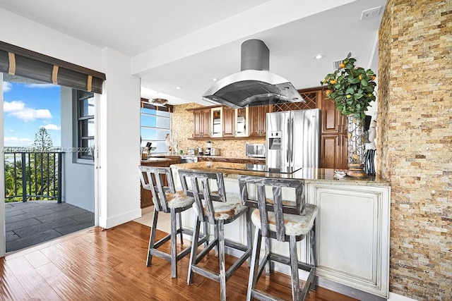 kitchen featuring island exhaust hood, kitchen peninsula, light hardwood / wood-style flooring, stainless steel appliances, and decorative backsplash