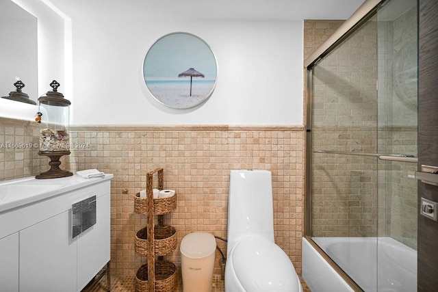 full bathroom featuring tile walls, combined bath / shower with glass door, vanity, and toilet