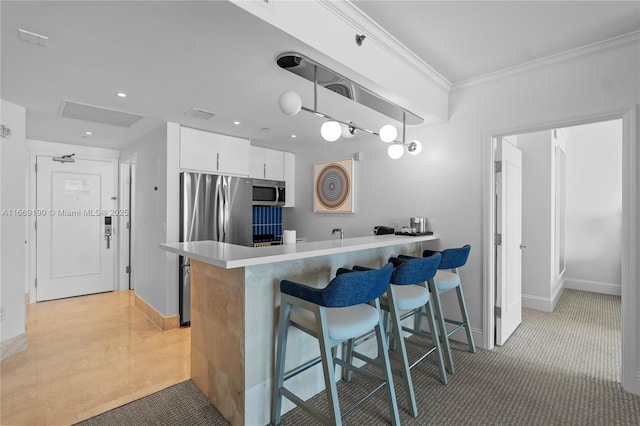 kitchen featuring kitchen peninsula, appliances with stainless steel finishes, a breakfast bar, decorative light fixtures, and white cabinets